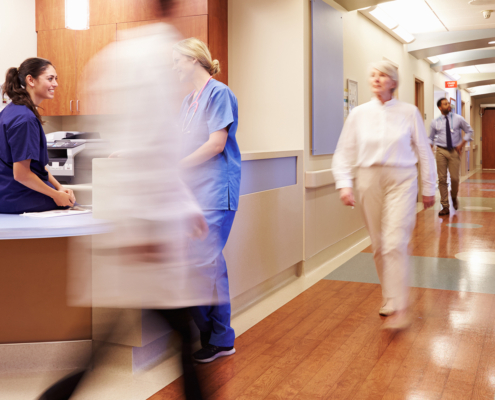 Hospital setting with multiple people walking down hallway indicating hurriedness and motion