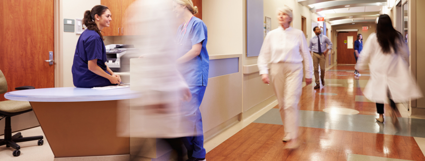 Hospital setting with multiple people walking down hallway indicating hurriedness and motion