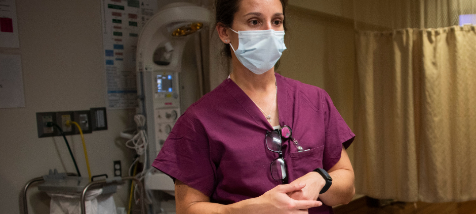Provider in maroon scrubs looks to patient out of frame with mask on, she's in a clinical setting